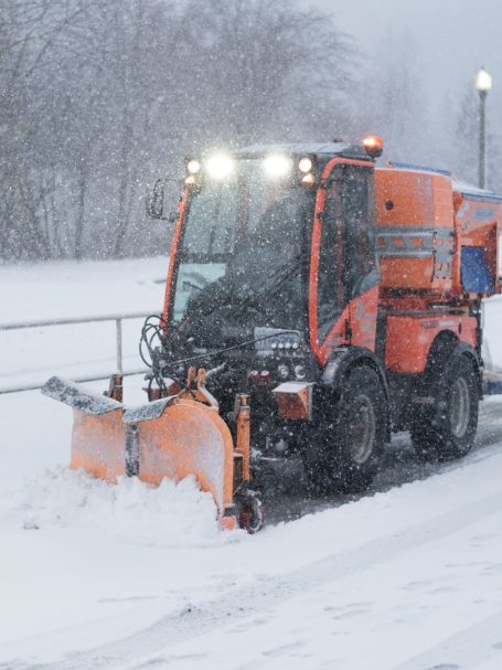 Ein orangefarbener Schneepflug räumt bei Schneefall eine Straße frei.