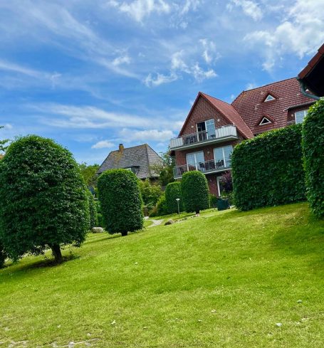 Grüne Rasenlandschaft mit gepflegten Bäumen und mehreren Wohnhäusern im Hintergrund.