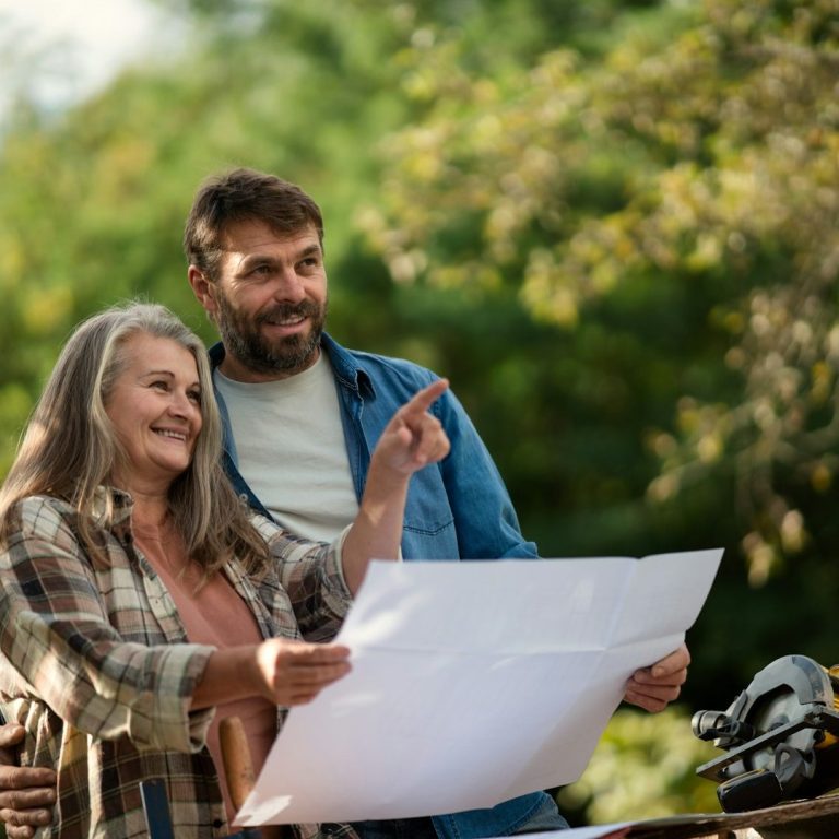 Zwei Personen betrachten einen Plan im Freien und lächeln sich an.