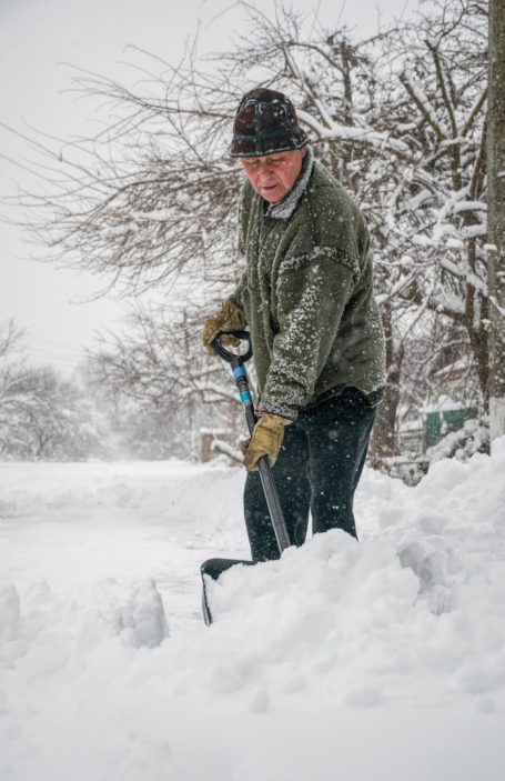 Mann schaufelt Schnee in einer verschneiten Umgebung.